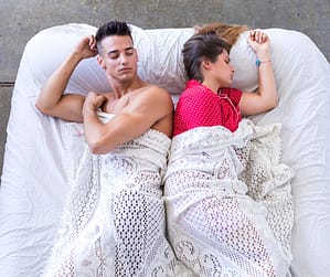 Husband and wife lying apart under blankets, a sign of distance, showing loss of sexual desire in marriage, that fits how to fix a sexless marriage and how to rekindle desire in a long-term marriage when mismatched libido in marriage hurts intimacy.