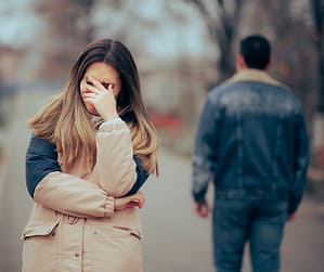 A woman cries after a breakup as her partner walks away, showing she’s not healed from past relationships and still carrying unhealed relationship trauma.