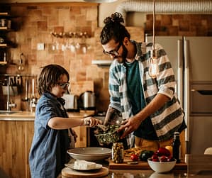 Single dad cooking with his son in a home kitchen, illustrating How does single parenting affect a child by building confidence, responsibility, and a stable daily bond.