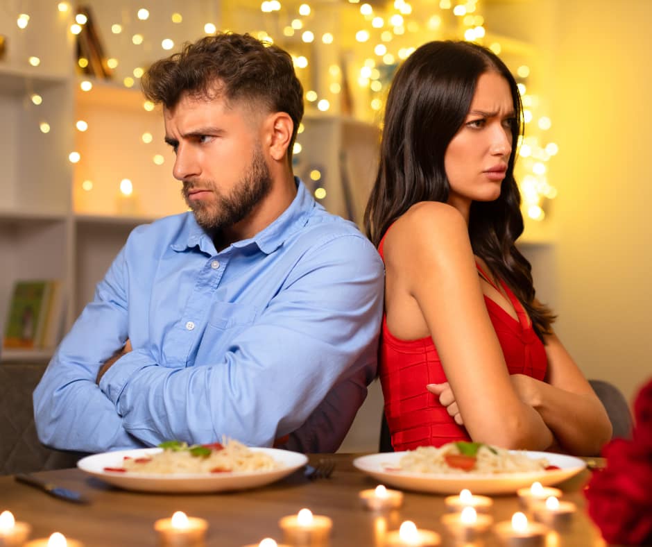 Couple sits back-to-back at a candlelit dinner, arms crossed and upset after an argument—breakup trauma isn't healing and the distance feels permanent